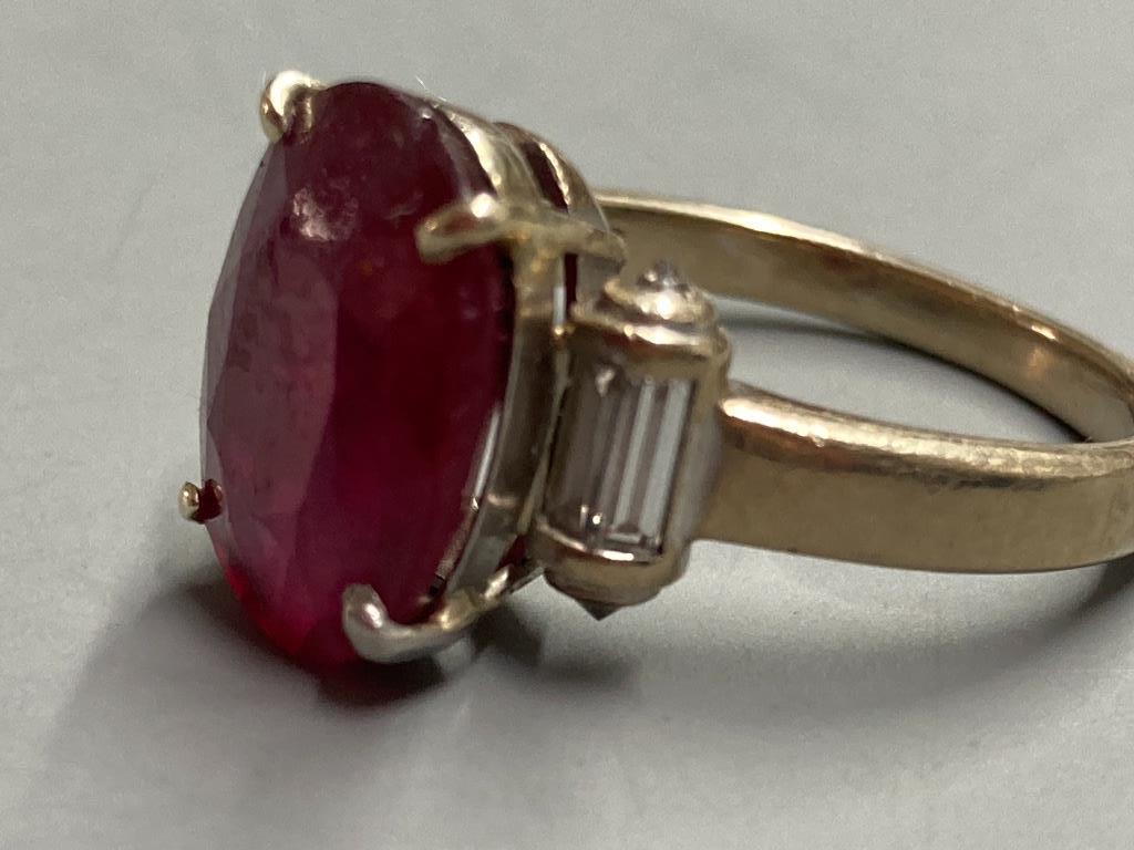 A modern yellow metal (stamped 750) and oval cut single stone ruby dress ring, with baguette cut diamond set shoulders